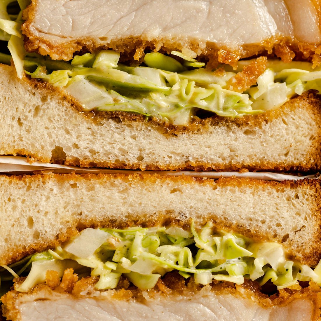 Cross-section of a crumbed fried chicken toastie layered with slaw between thick slices of bread
