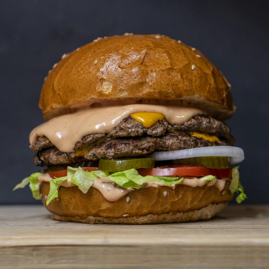 Double smashed beef burger with cheese, pickles, tomato and onion on a sesame bun